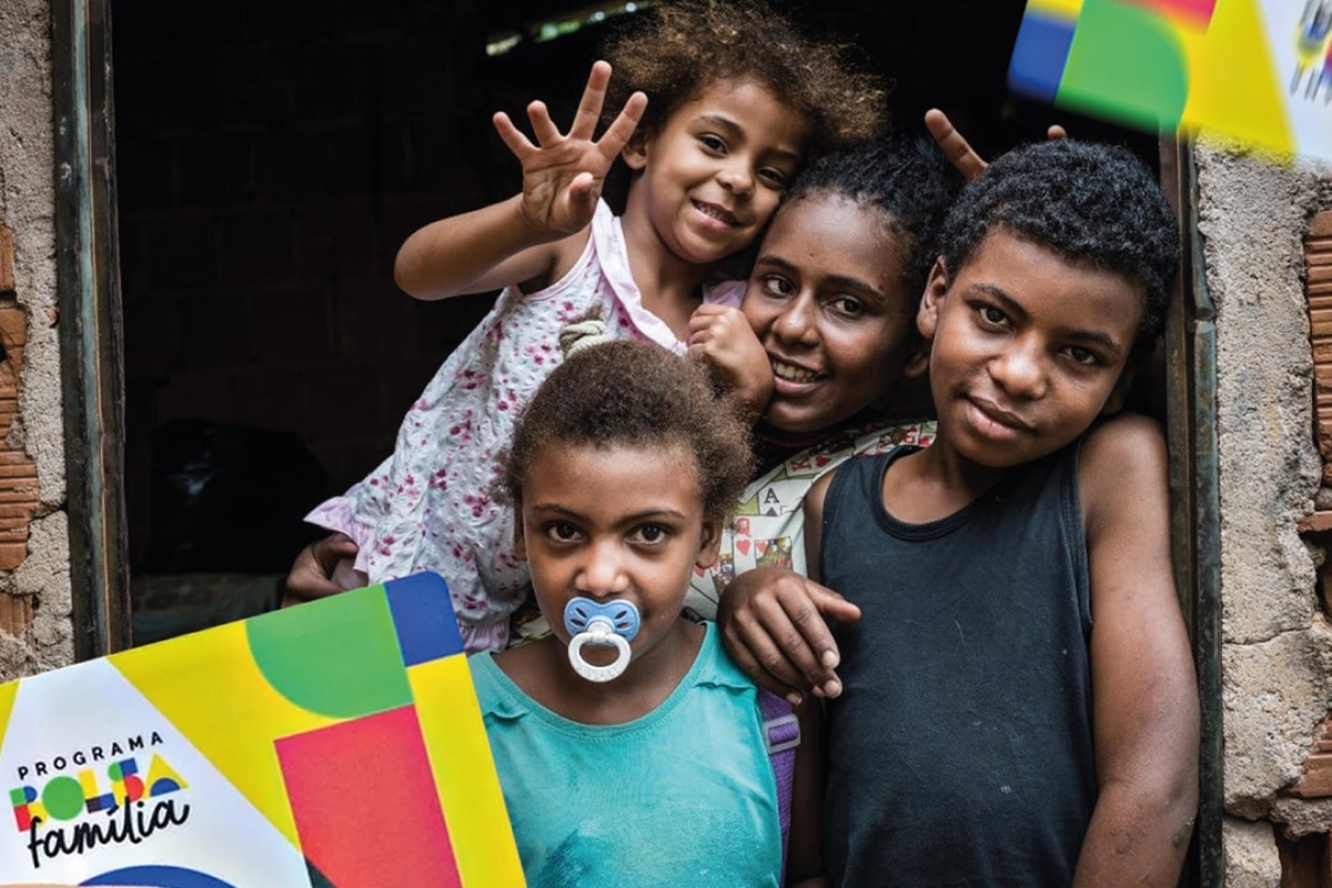 Família com crianças sorrindo e segurando o cartão do Bolsa Família, simbolizando o apoio financeiro do programa