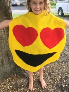 Criança vestida com uma fantasia caseira de emoji de olhos apaixonados, sorrindo e se divertindo ao ar livre