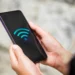 Pessoa segurando um smartphone exibindo o símbolo de Wi-Fi, representando a conectividade sem fio