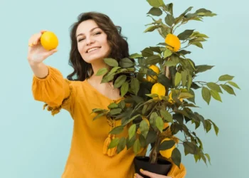 Mulher sorrindo e segurando uma árvore de limão cultivada em vaso, simbolizando a facilidade de cultivar frutas em espaços pequenos.