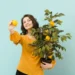 Mulher sorrindo e segurando uma árvore de limão cultivada em vaso, simbolizando a facilidade de cultivar frutas em espaços pequenos.