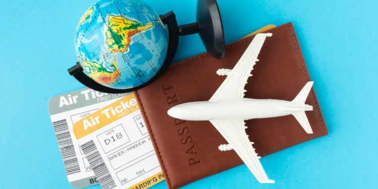 Passagem aérea, modelo de avião de plástico e globo terrestre com passaporte sobre fundo azul.