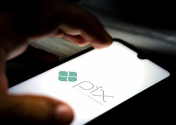 Imagem mostrando o logo do Pix, sistema de pagamentos instantâneos, com foco na tela de um celular em um ambiente escuro.