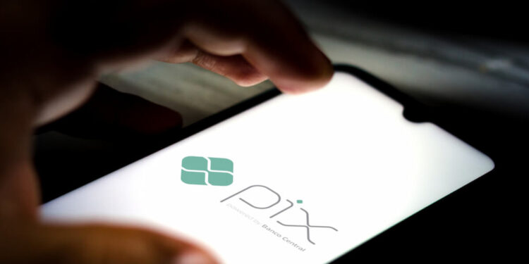Imagem mostrando o logo do Pix, sistema de pagamentos instantâneos, com foco na tela de um celular em um ambiente escuro.