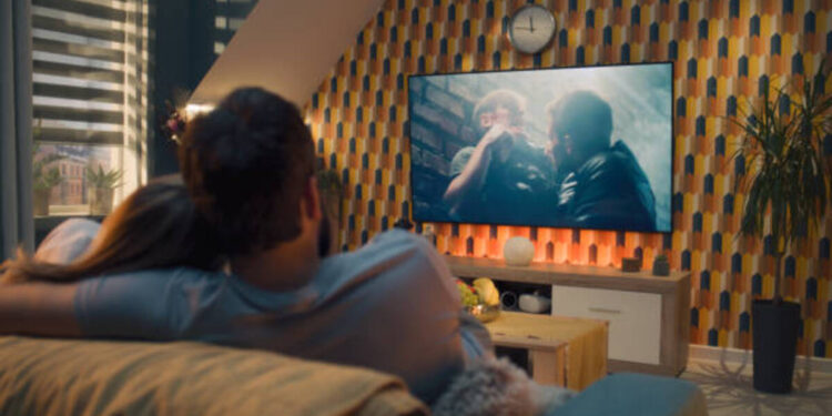 Casal assistindo uma cena emocionante de série turca em TV grande no sofá.